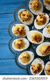 Deviled eggs in a clear decorative glass dish on a blue wooden surface