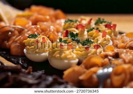Deviled eggs garnished with herbs and peppers, served alongside smoked salmon on a gourmet buffet. Close-up of elegant deviled eggs and salmon appetizers at a luxury catering event.