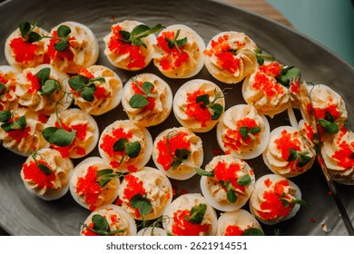 Deviled eggs topped with red caviar and fresh greens, artfully arranged on a serving tray for a gourmet buffet or catered event.