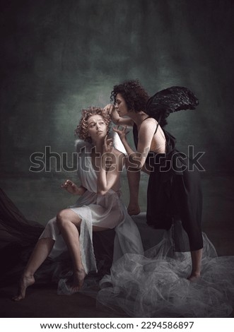 Devilish woman whispering to naive angel. Portrait of two women, angel and demon against dark, green, vintage background. Concept of history, remake, good and bad, creative photography