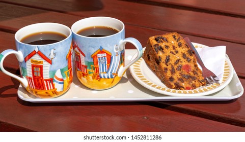 Devon, England, UK. July 2019. Fruit Cake On A Plate With Two Decorated Cups Of Black Coffee On A Tray