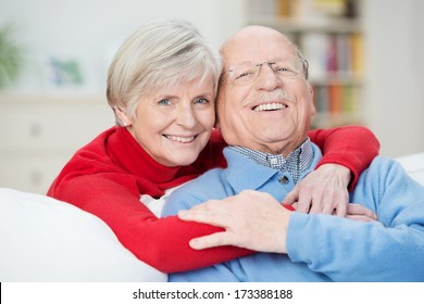 Devoted happy senior couple sitting in a close embrace on a sofa in the living room relaxing and laughing