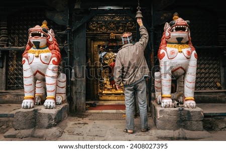 A devotee rings the bell at the entrance of a Kathmandu temple, flanked by mythic lion statues symbolizing protection and tradition