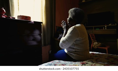 Devout Christian Senior African American Woman in Prayer at Home, seated by bedside in bedroom. One black lady in 80s and gray hair in deep meditation, solitude Prayer - Powered by Shutterstock