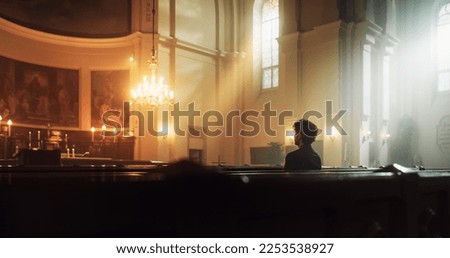 A Devout Christian Sits Piously In A Grand Church, Folding Hands for Praying, Contemplating Their Earthly Life. Parisher Seeks Moral Guidance From the Faith. Religious Atmosphere Of The Sacred Space 商業照片 © 