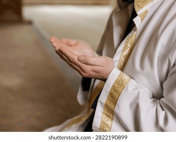 Devout religious man wearing traditional white robes holds his open hands up during daily sincere prayer