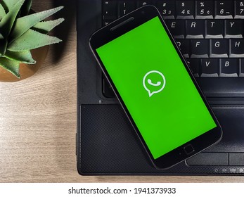 Brasília - DF, Brazil. March 23, 2021: Whatsapp app the on smartphone screen with Notebook on wood background. WhatsApp is a multi platform instant messaging and voice calling app for smartphones.