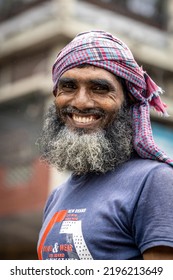 DHAKA, BANGLADESH - AUGUST 27, 2022: Close Up Portrait With A Blurred Background Of A Smiling South Asian Worker With A Grey Beard And A Bandana Around His Head