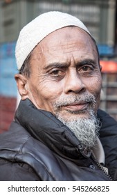 DHAKA, BANGLADESH - DECEMBER 30, 2016: An Older Muslim Man With A White Tupi And A Grey Beard And A Black Jacket Is Feeling Cold In Winter.