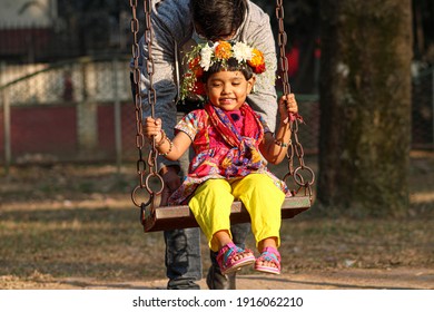 Dhaka, Bangladesh: February 13, 2021: Adorable Little Kid Is Swinging Backed By His Father  Celebrating First Day Of Spring, Selective Focus