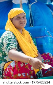 DHAKA, BANGLADESH - MAY 15, 2021: Portrait Of A South East Asian Indian Or Bangladesh Lady Sitting With A Colorful Yellow Head Scarf Next To A Bright Blue Boat