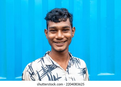 DHAKA, BANGLADESH - SEPTEMBER 15, 2022: Street Photography Portrait Of A Smiling Young Indian Looking Man With Black Hair Standing In Front Of A Blue Background