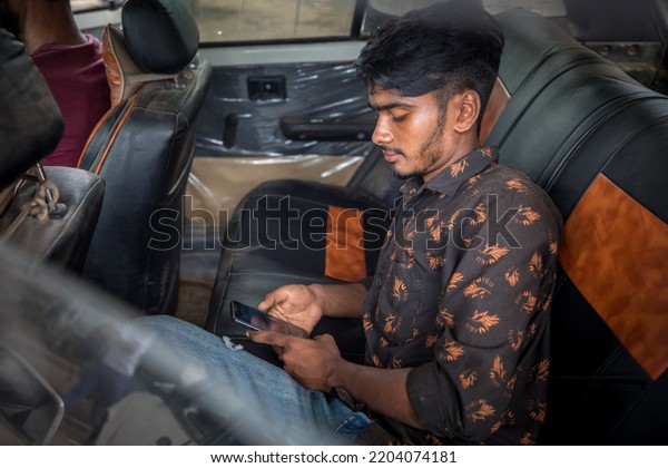 DHAKA, BANGLADESH - SEPTEMBER 15, 2022: Street\
photography portrait of a young guy sitting in the back of a car\
and playing with his mobile\
phone