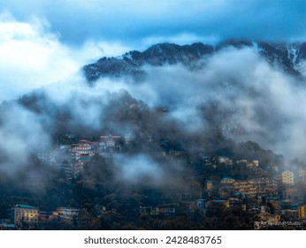 Dharamshala : Misty mountains cradle Dharamshala. Wispy fog dances around snow-kissed peaks, shrouding the vibrant town below. Sunlight peeks through, casting an ethereal glow on rooftop - Powered by Shutterstock