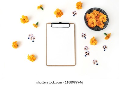 Dia de los Muertos, Mexican Day of the Dead composition. Clipboard, blank paper mockup, orange tagetes, marigold flowers and decorative paper skull stickers, white table background. Flat lay, top view