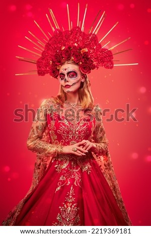 Dia de los Muertos. Santa Muerte. Beautiful Calavera Catrina in a festive rich dress and headdress stands on a red background. Sugar skull girl. Day of The Dead. Halloween.