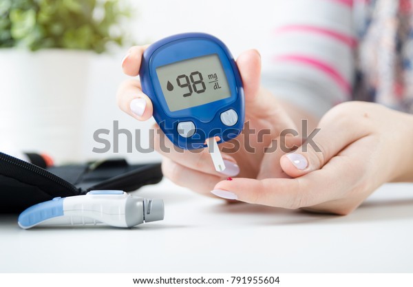 Diabetes checking blood sugar level. Woman using\
lancelet and glucometer at\
home.