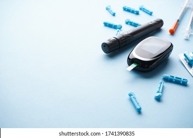 Diabetes concept, medical technology. Digital glucometer, lancet pen and syringes on blue background with space for text. 
