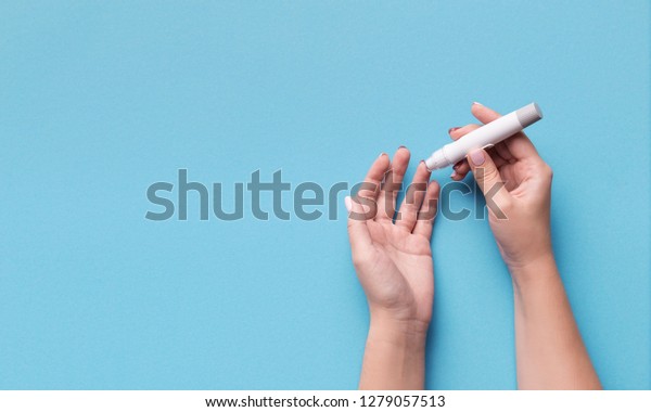 Diabetes test. Woman hands\
checking blood sugar level by Glucose meter on blue background,\
copy space