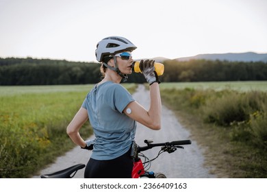 Diabetic cyclist with a continuous glucose monitor on her arm drinking water during her bike tour. - Powered by Shutterstock