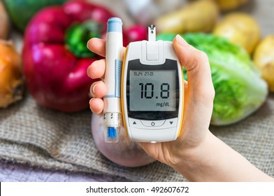 Diabetic Diet And Diabetes Concept. Hand Holds Glucometer. Vegetables In Background.