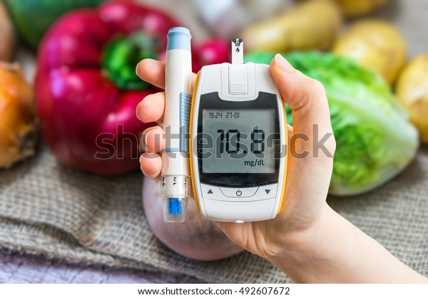 Diabetic diet and diabetes concept. Hand\
holds glucometer. Vegetables in\
background.