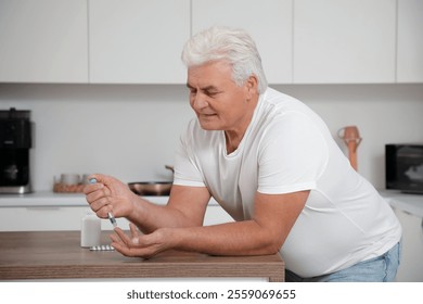 Diabetic mature man using lancet pen at table in kitchen - Powered by Shutterstock