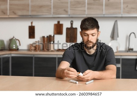 Diabetic young man using glucometer in kitchen
