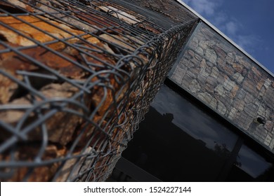 Diagonal composition of building construction element of stone with steel net hardening and glass panel with blue sky on background.