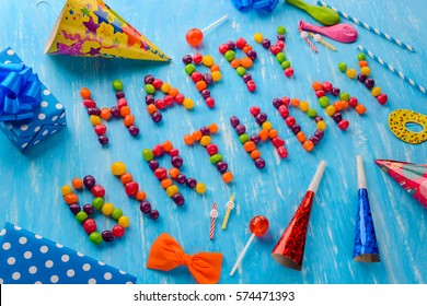 Diagonal Happy Birthday sign made of jelly beans. A yellow party hat, noisemakers, an orange paper bow, red lollipops, small candles on the blue background. For a special mood. - Powered by Shutterstock