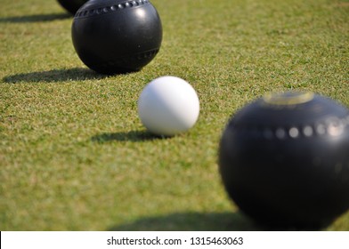 Diagonal Line Of Black Lawn Bowls And A White Jack On Green Turf. 