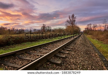 Diagonal railway tracks in a rural scene leading into distant colorful sunset.