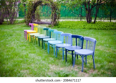 Diagonal Row Of Colorful Wooden Chairs On The Lawn In The Backyard, Preparing For A Micro Wedding Ceremony. 