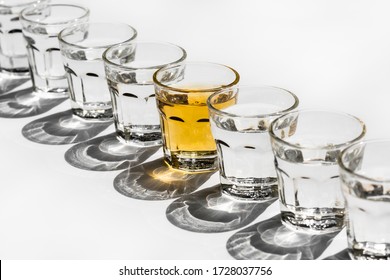 Diagonal Row of Shot Glasses on a White Background, with Shadows and One Orange Shot in the Middle