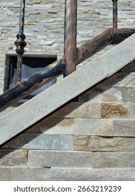 Diagonal view of three main objects: hand-forged metal railing, polished stone stairs, and textured wall tiles. The staircase runs bottom left to top right. Warm daylight highlights surface textures