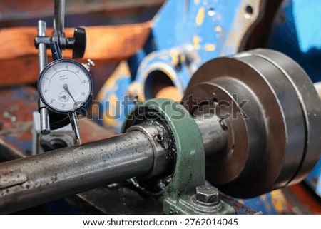 Dial test indicator measuring shaft runout on industrial machinery in a workshop. Precision tool checking mechanical rotation accuracy on steel metal part.