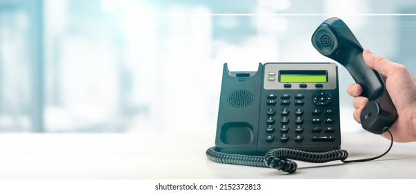 Dialing Landline Telephone Keypad Concept For Communication, Contact Us And Customer Service Support. Hand Holding Voip Telephone Receiver On Blurred Office Background. Banner