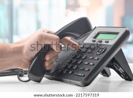 Dialing voip telephone keypad concept for communication, contact us and customer service support. landline telephone device at office desk. hand dialing number and holding telephone receiver