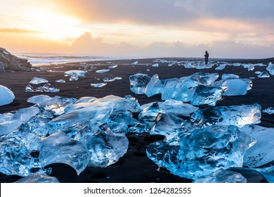 Diamond Beach in Iceland with blue icebergs melting on the black sand and ice glistening with sunrise sun light, tourist looking at beautiful arctic nature scenery, Icelandic South coast, Jokulsarlon