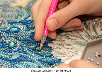 Diamond painting embroidery craft. Acrylic rhinestones and hand holding a pen. Closeup, selective focus.