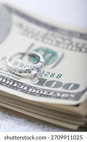 Diamond ring resting on a stack of hundred dollar bills at a luxury setting