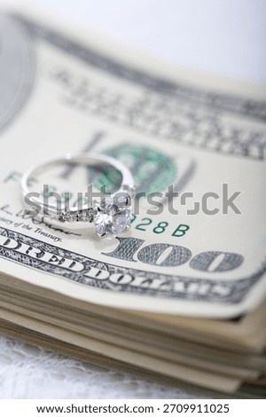 Diamond ring resting on a stack of hundred dollar bills at a luxury setting