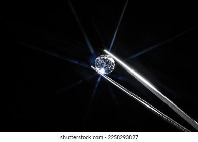 Diamond selective focus held in metal jeweller tweezers, brilliant stone cut with star shape light ray burst, starburst or sunbeam. Inspection of polish quality and contamination. Carbon material. - Shutterstock ID 2258293827