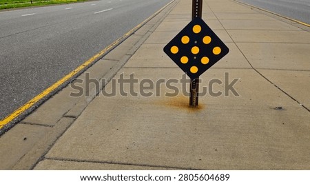 Diamond shaped object marker sign with reflective circles on a concrete sidewalk median separating traffic lanes. Infrastructure background.