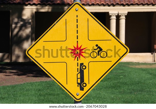 Diamond shaped yellow\
collision warning traffic sign depicting a car and a bicycle and a\
red flashpoint