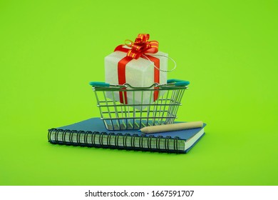 Diary or spiral bound notebook with shopping basket, pencil and gift with colorful red ribbon over green with copy space in a conceptual image - Powered by Shutterstock