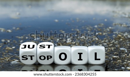Dice form the expression 'just stop oil' in front of an lake full of oil.