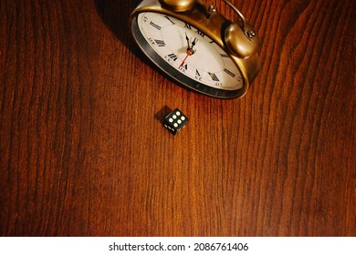 a dice on a brown table near the alarm clock set at 12 o'clock