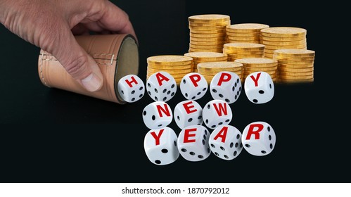 Dice Spelling Happy New Year When Tumbling Out Of A Raffle Cup Hold By One Hand  With Stacks Of Golden Coins On Black Background. Good Luck And Wealth Concept.