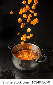 Diced Pumpkin Falling In A Boiling Pot, Isolated Black Background With Water Splash